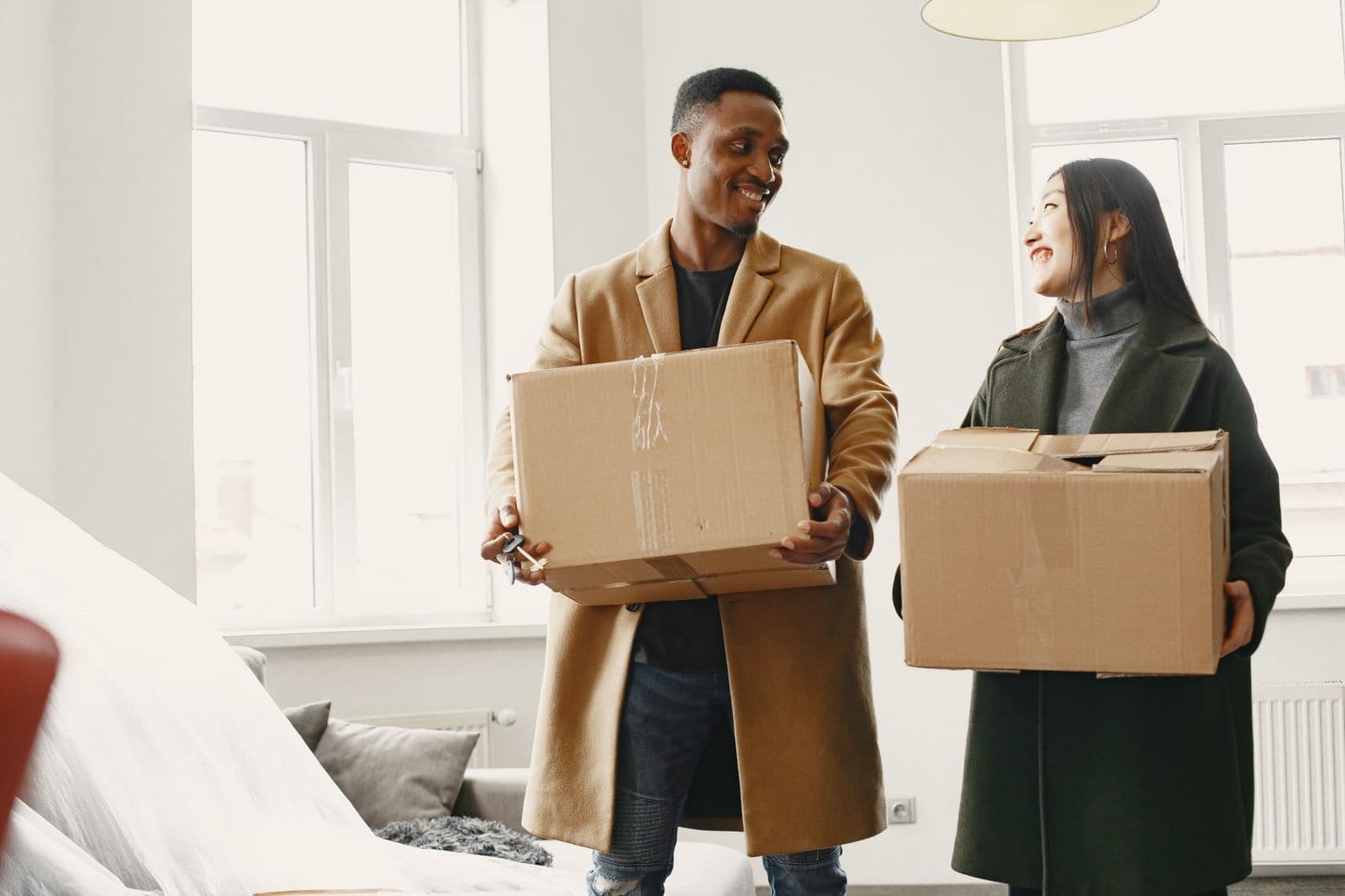 Pareja sonriente cargando cajas de mudanza al apartamento nuevo